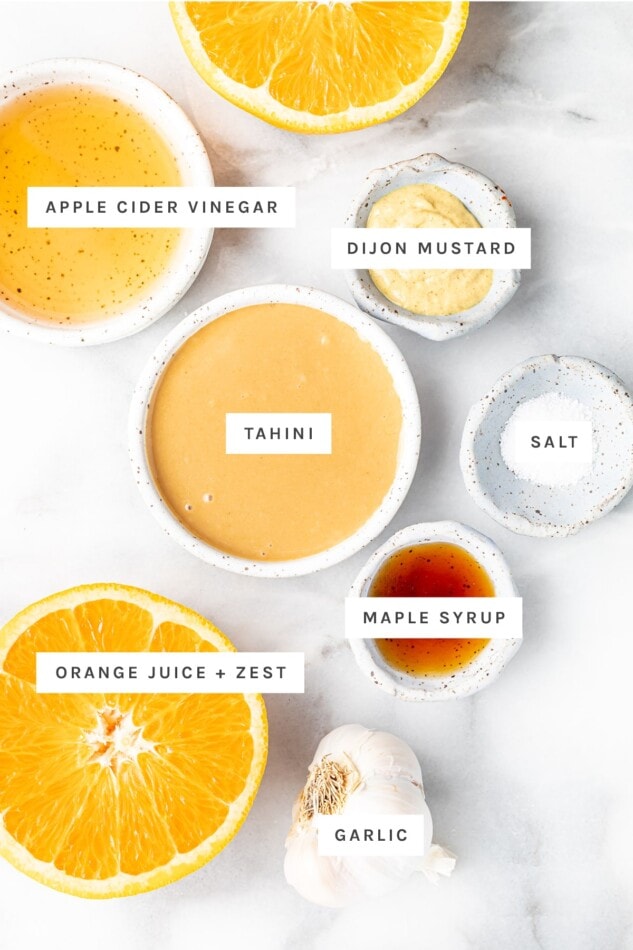 Ingredients measured out to make citrus tahini dressing: apple cider vinegar, dijon mustard, tahini, salt, maple syrup, orange juice and zest and garlic.