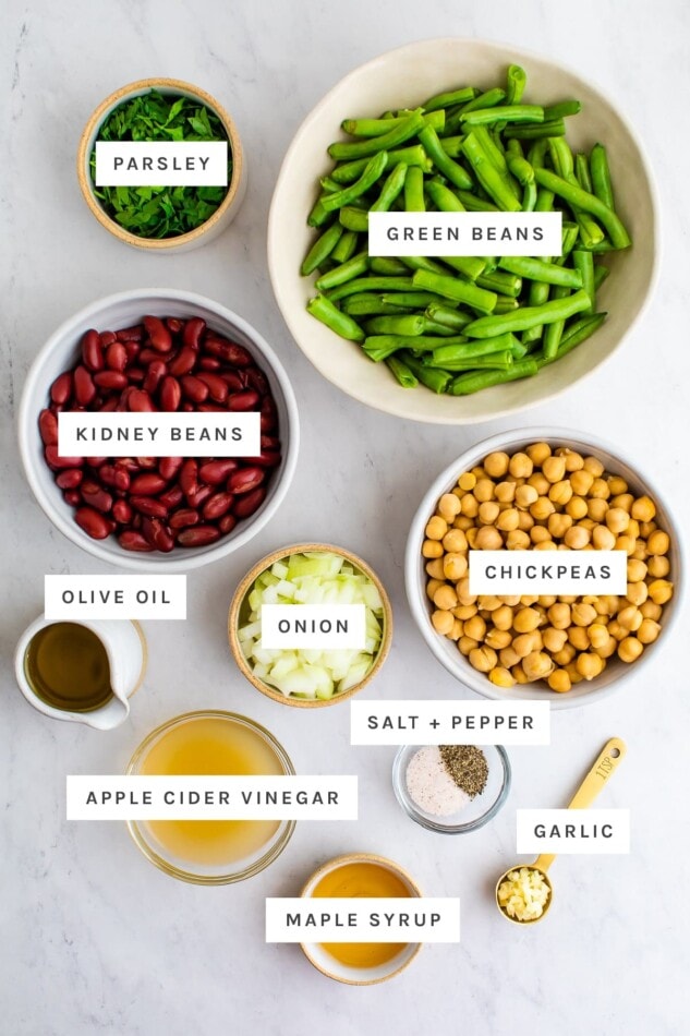 Ingredients measured out to make three bean salad: parsley, green beans, kidney beans, chickpeas, olive oil, onion, salt, pepper, vinegar, garlic and maple syrup.