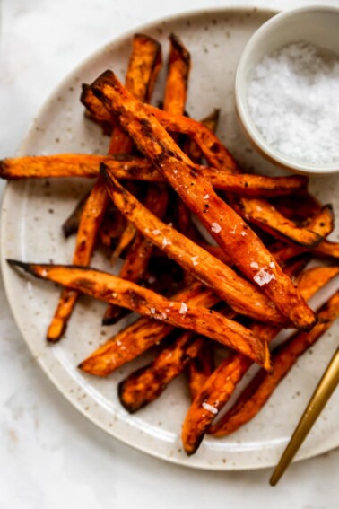 Overhead shot of a plate with fries, there is a ramekin of salt in focus.