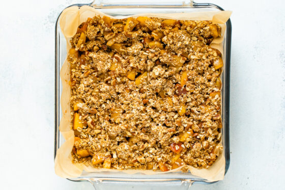 A glass baking pan lined with parchment paper and filled with apple crumble filling before being baked.