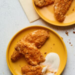 Overhead shot of baked chicken tenders on 2 plates with dipping sauce.