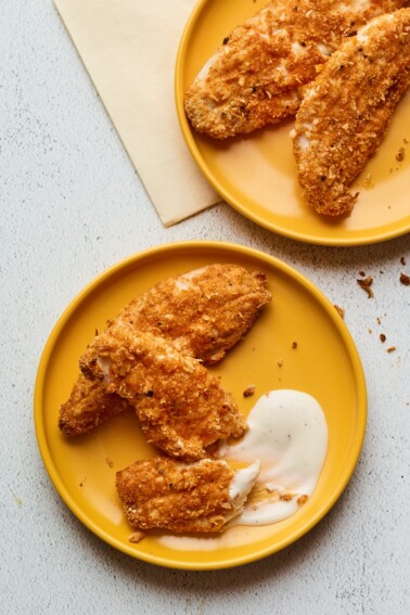 Overhead shot of baked chicken tenders on 2 plates with dipping sauce.