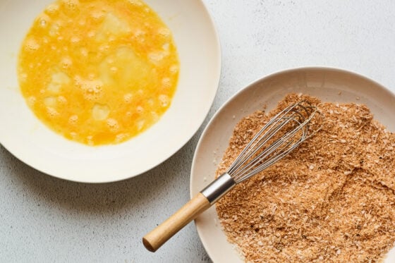 Overhead shot of two bowls. One bowl has eggs that have been whisked and the second bowl has a mixture of dry ingredients with a whisk resting in the bowl.