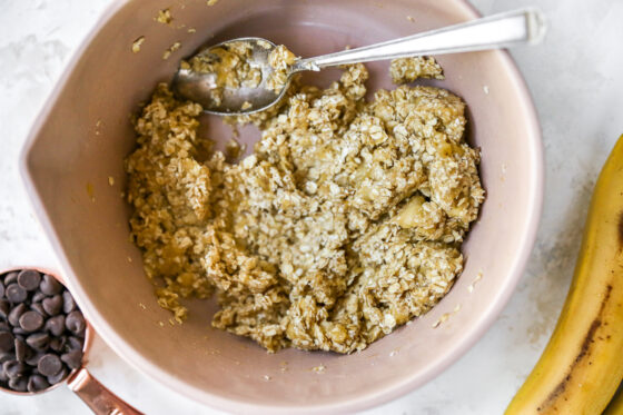 Banana and oats mixed together inside of a bowl with a silver spoon.