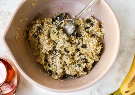 A mixing bowl with the ingredients for banana cookies all mixed together. There is a silver spoon resting inside the bowl.