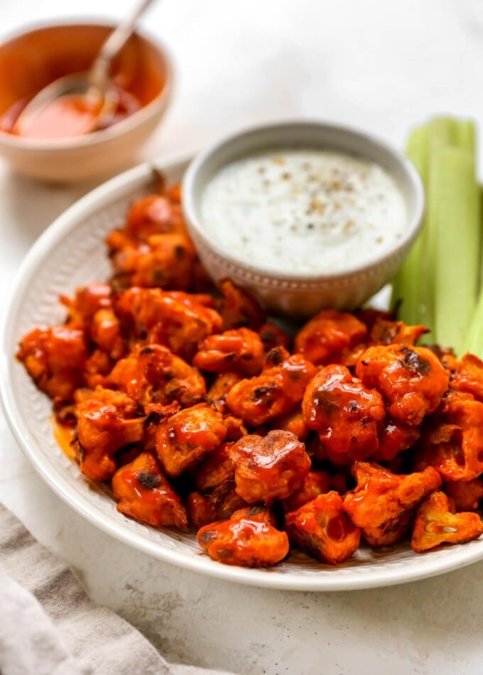 Plate of buffalo cauliflower wings served with vegan cashew ranch and celery sticks.