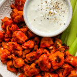 Plate of buffalo cauliflower wings served with vegan cashew ranch and celery sticks.