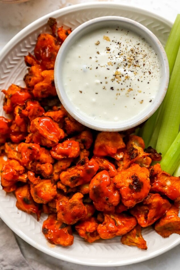 Plate of buffalo cauliflower wings served with vegan cashew ranch and celery sticks.