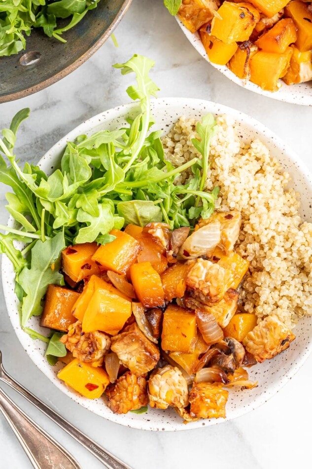 Butternut squash tempeh bake served with brown rice and greens in a shallow bowl.