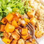 Overhead view of butternut squash tempeh bake served with brown rice and greens, a fork is scooping a bite.