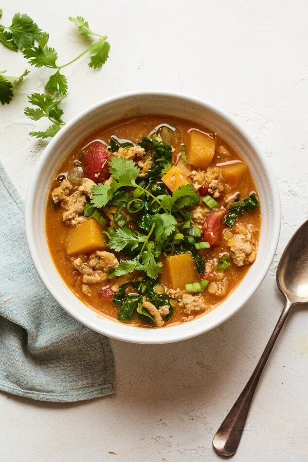 An overhead shot of a bowl of butternut squash turkey chili. A silver spoon rests to the side of the bowl.