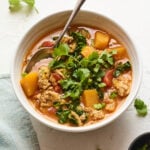 A bowl of butternut squash turkey chili with cilantro on top. A silver spoon rests inside the bowl of chili.