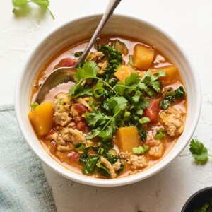 A bowl of butternut squash turkey chili with cilantro on top. A silver spoon rests inside the bowl of chili.