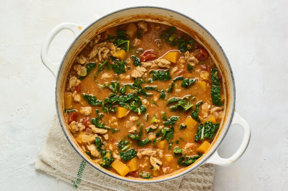 Chopped kale added to a large pot with vegetables and ground turkey.