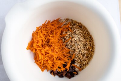 A bowl containing carrots, pecans, and raisins ready to be combined.