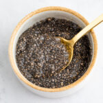 A small ceramic bowl with chia seeds and water mixture. A spoon is lifting some out.