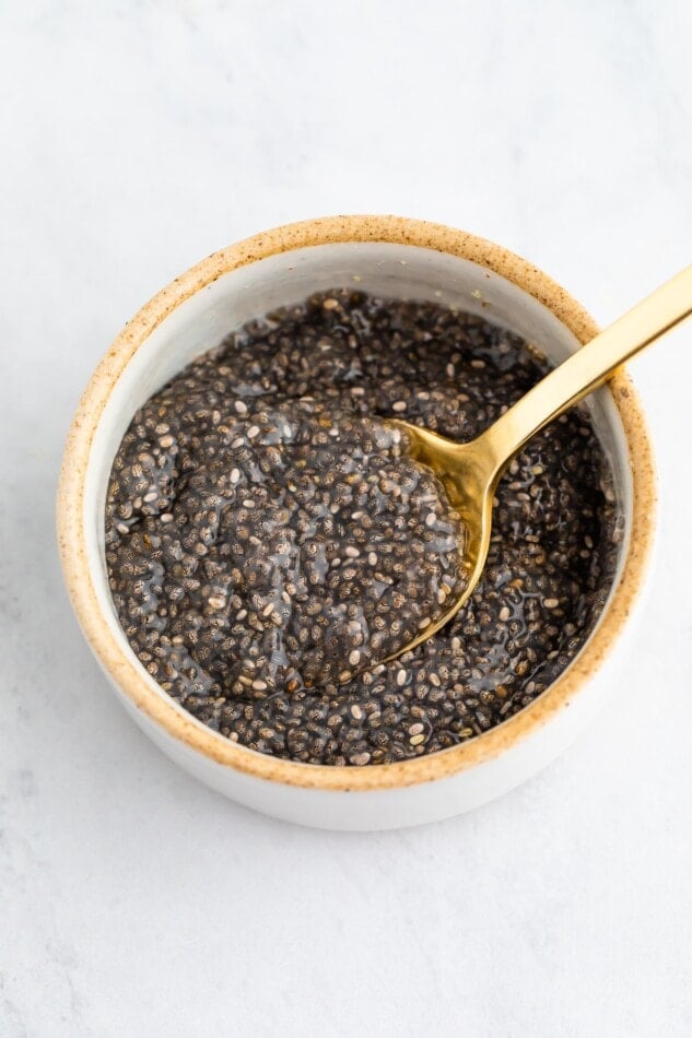 A small ceramic bowl with chia seeds and water mixture. A spoon is lifting some out.