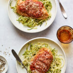 An overhead shot of two bowls of zucchini noodles with a chicken breast resting on top of each.
