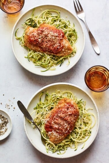 An overhead shot of two bowls of zucchini noodles with a chicken breast resting on top of each.