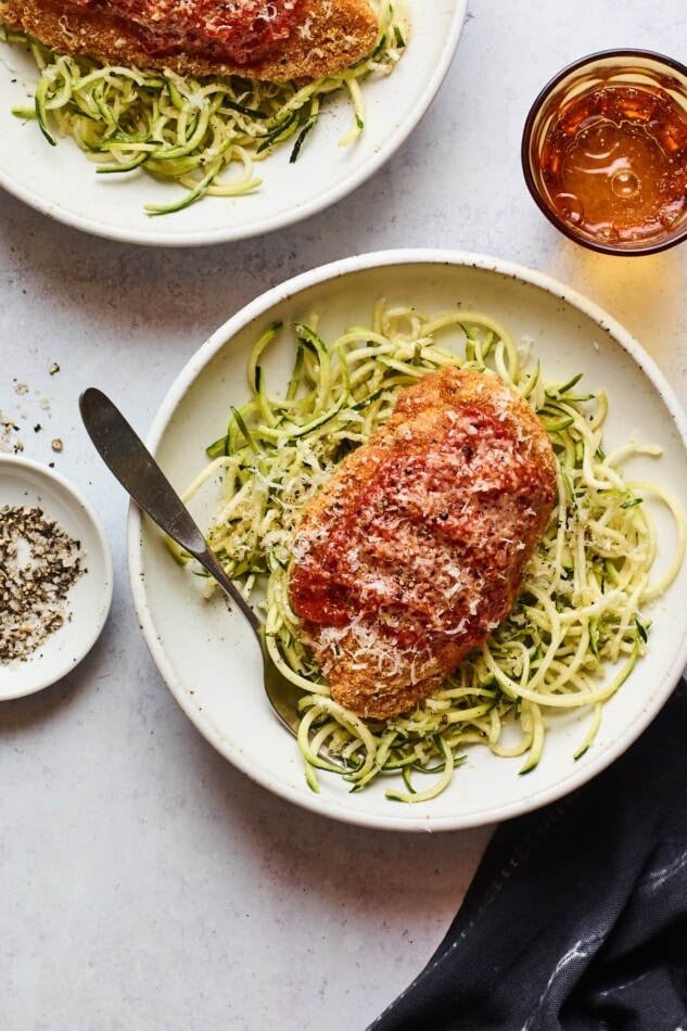 Overhead shot of a bowl of zucchini noodles with a chicken parm breast resting on top. There is a second bowl partially in the frame.