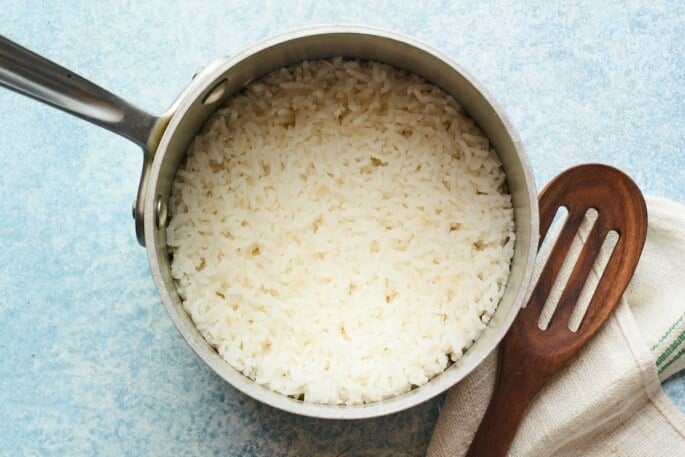 Overhead shot of cooked rice in a pot with a slated spoon.