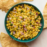 Easy corn salsa served in a blue bowl with crispy tortilla chips scattered around the bowl.