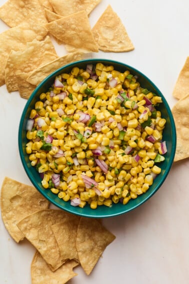 Easy corn salsa served in a blue bowl with crispy tortilla chips scattered around the bowl.