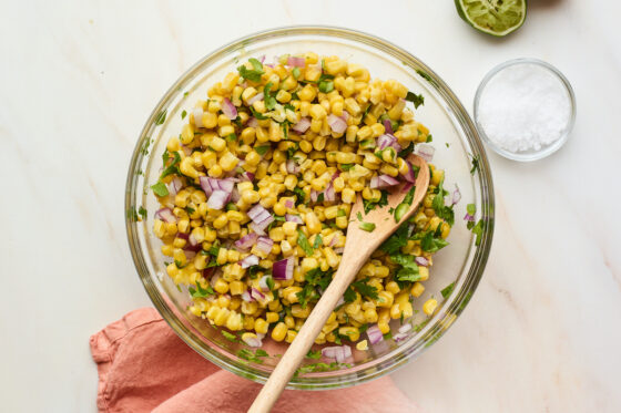 Corn salsa in glass mixing bowl with wooden mixing spoon.