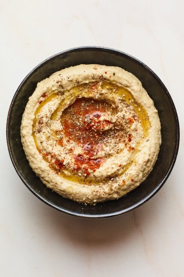 Creamy hummus with olive oil and spices on top in a black serving bowl.