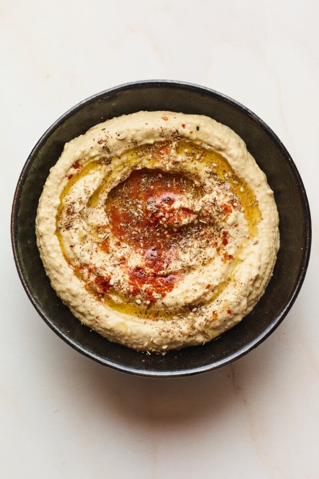 Creamy hummus with olive oil and spices on top in a black serving bowl.