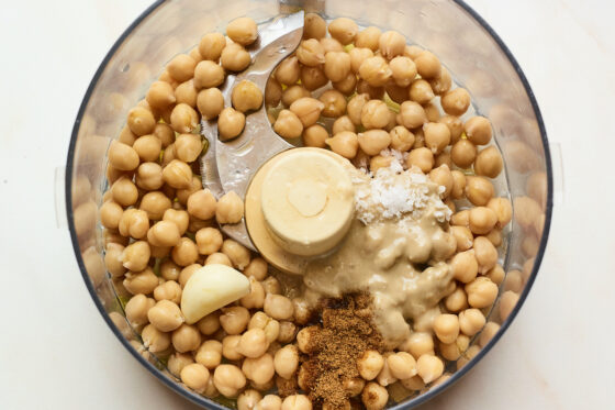 Chickpeas, tahini, garlic, salt, lemon juice, and olive oil in a food processor ready to be blended.