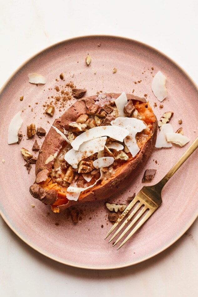 An overhead shot of a dessert sweet potato with topping sprinkled around. A gold fork rests on the plate next to the potato.