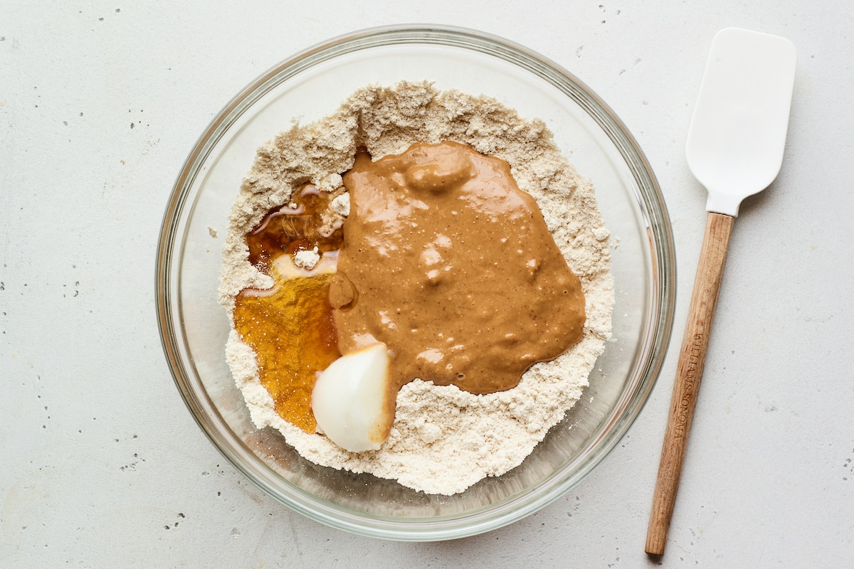 Protein powder, honey and peanut butter in a bowl. Spatula is beside the bowl.