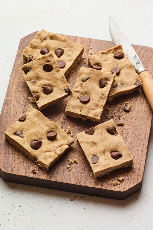 Chocolate chip peanut butter protein bars on a wood cutting board with a knife.