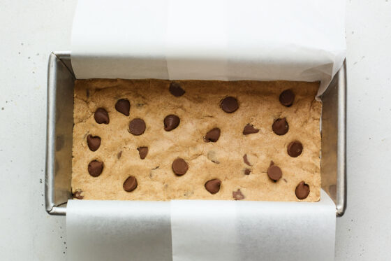 Chocolate chip peanut butter protein bar mixture in a loaf pan lined with parchment.