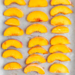 Frozen peaches in three columns on a parchment lined baking sheet