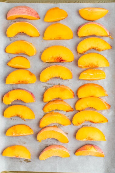 Frozen peaches in three columns on a parchment lined baking sheet