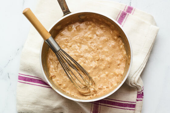 Almond milk, peanut butter, maple syrup, cocoa powder and sea salt mixture bubbling in a pot with a whisk.