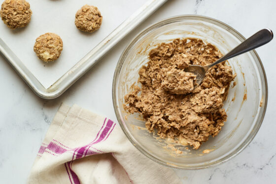 Cookie sheet with no bake protein cookies next to a mixing bowl with the cookie mixture and a spoon.