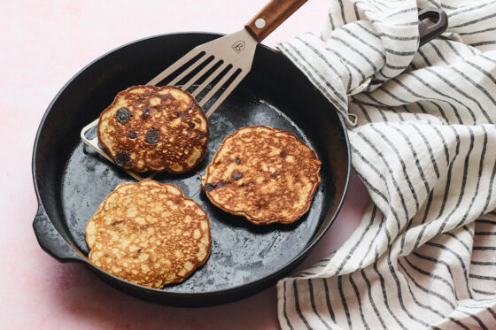 Cast iron skillet with three protein pancakes and a spatula lifting one up.