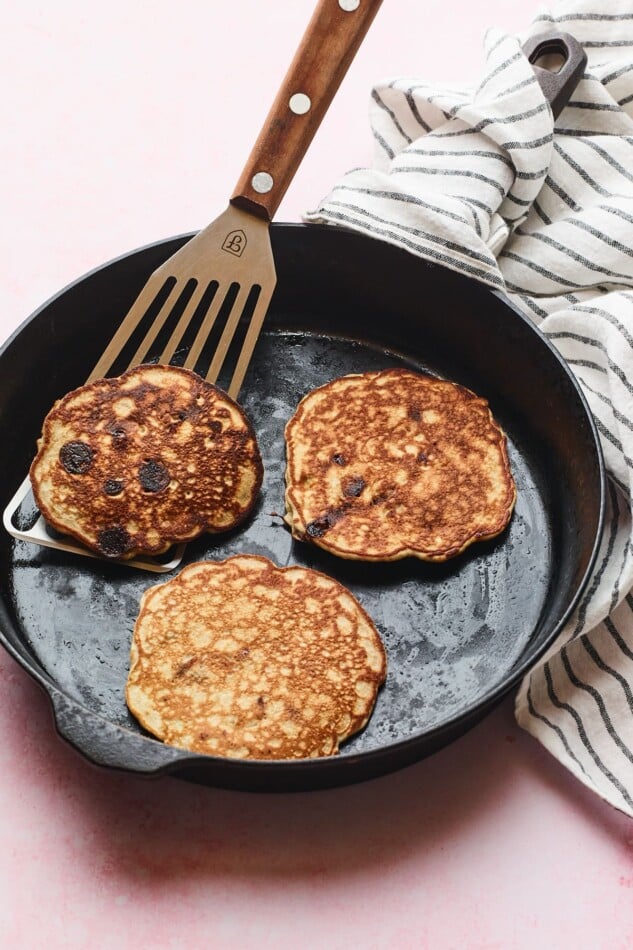 Cast iron skillet with three protein pancakes and a spatula lifting one up.