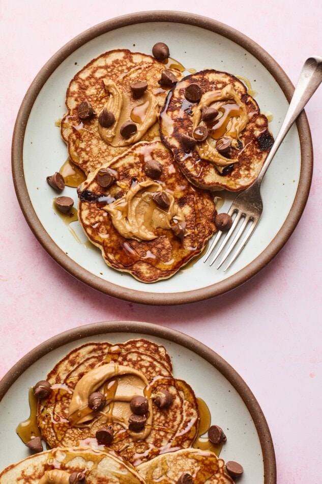 Two plates with protein pancakes topped with maple syrup, peanut butter and chocolate chips.
