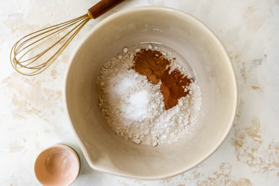A bowl of dry ingredients. A whisk is pictured, ready to mix them together.