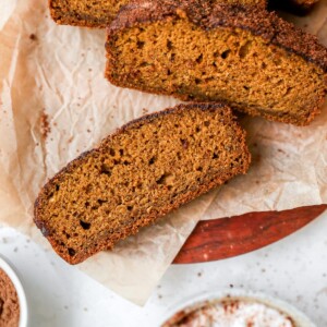 Overhead shot of four slices of pumpkin bread, resting on parchment paper on a cutting board.