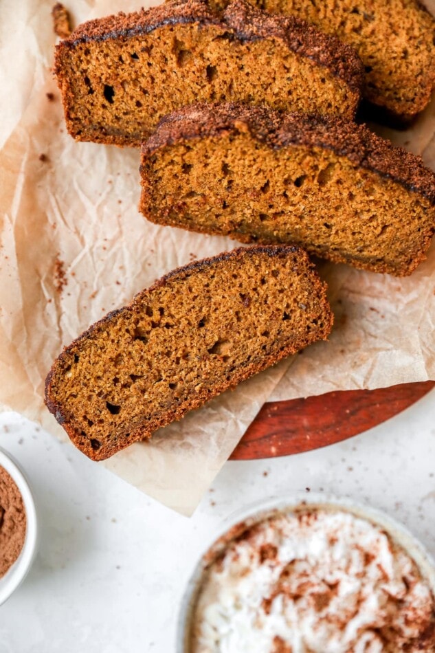 Overhead shot of four slices of pumpkin bread, resting on parchment paper on a cutting board.