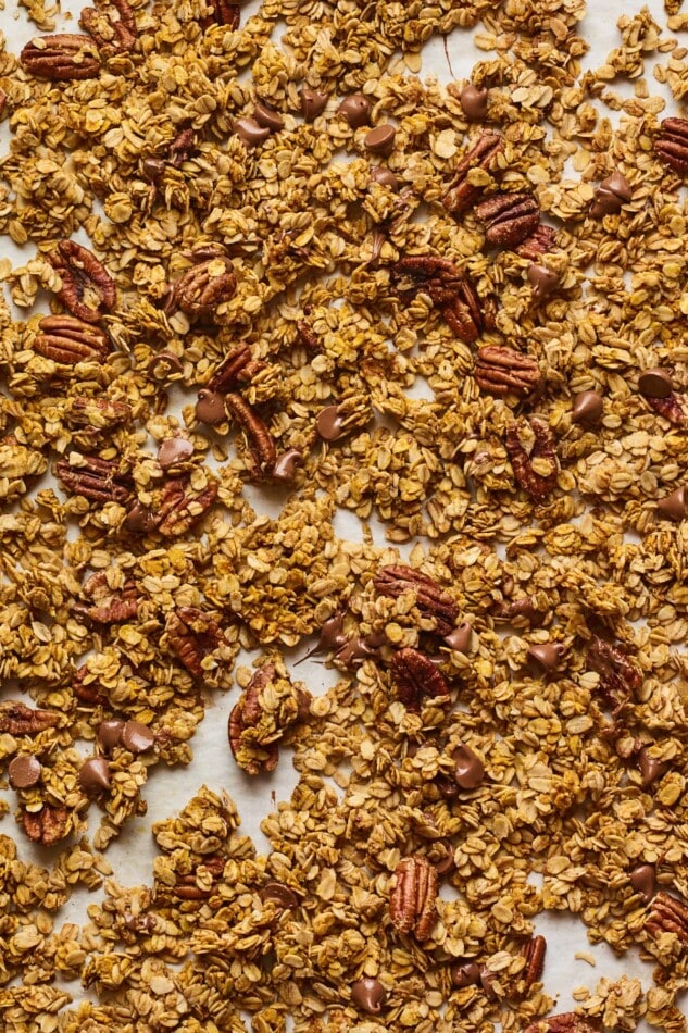 Sheet pan of baked pumpkin granola with melted chocolate chips sprinkled throughout.