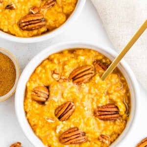 Overhead shot of two bowls of pumpkin oatmeal topped with pecans.