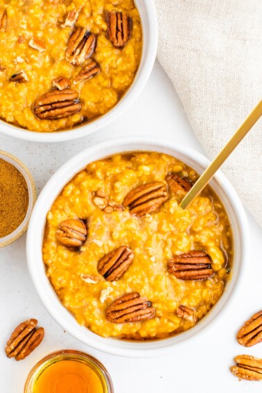 Overhead shot of two bowls of pumpkin oatmeal topped with pecans.