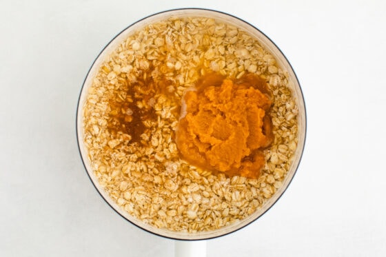 A white saucepan with ingredients for pumpkin oatmeal.
