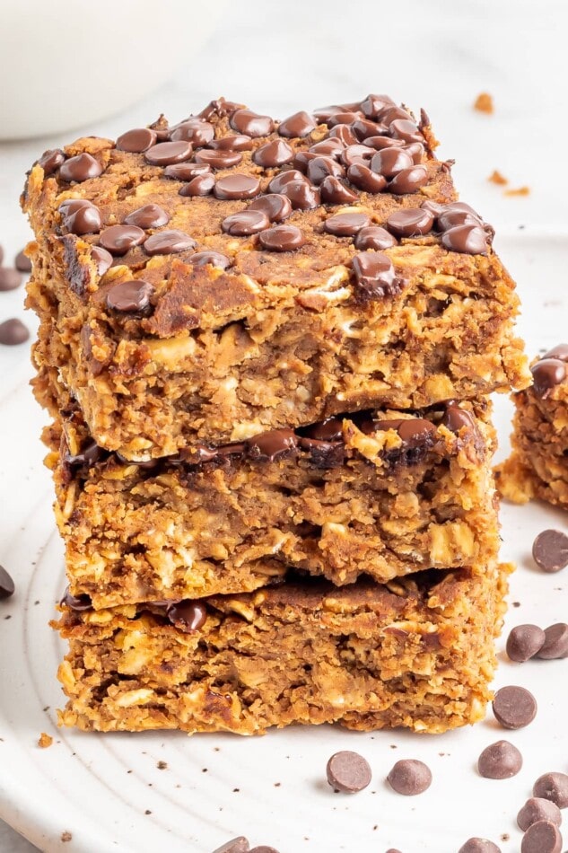 A stack of protein pumpkin bars on a white plate with chocolate chips sprinkled around.